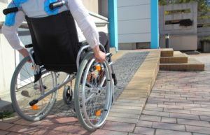 person in wheelchair using ramp to access the front door of a house
