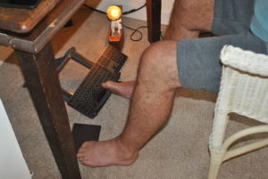 Peter using a pen held between his toes on his right foot to operate a computer keyboard and using his toes on his left foot to operate a tracking pad