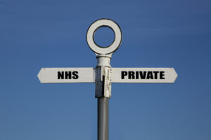 Old road sign with NHS and private pointing in opposite directions against a blue sky