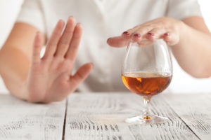 Woman refusing more alcohol by placing one hand over her glass and holding the other hand up to signify no more